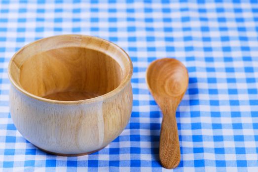 Wooden bowl, tablecloth, spoon, fork on table background