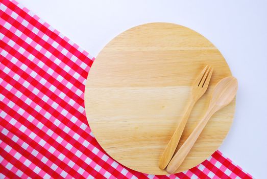 Wooden plate, tablecloth, spoon, fork on table background