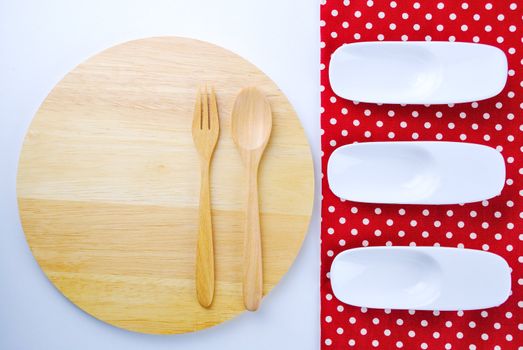 Wooden plate, tablecloth, spoon, fork on table background