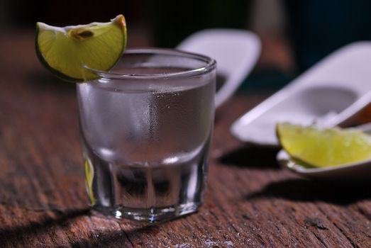 Glass of vodka shot with fresh lime on wooden table