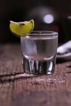 Glass of vodka shot with fresh lime on wooden table