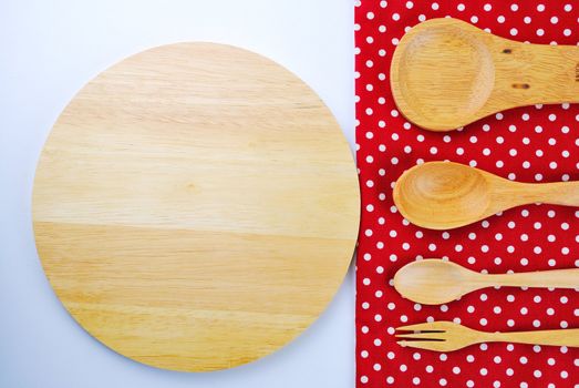 Wooden plate, tablecloth, spoon, fork on table background