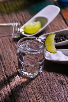 Glass of vodka shot with fresh lime on wooden table