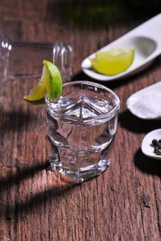 Glass of vodka shot with fresh lime on wooden table