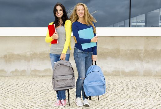 Two beautiful teenage students holding backpacks and smiling