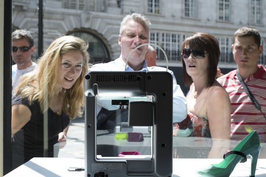 LONDON, UK - MAY 31: Pedestrians intrigued with 3D printer in United Nude shop window. The shop, based in Regent Street, has a line of products created on site by 3D printers. May 31, 2014 in London.