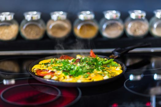 Omelet with vegetables on elecric stove and bowls with spices in the background of the kitchen.
