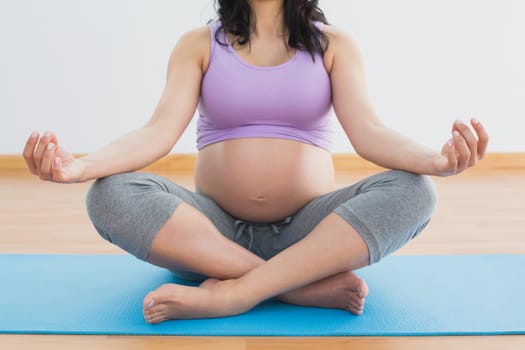 Pregnant brunette sitting on mat in lotus pose in a fitness studio