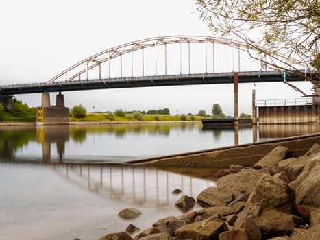 Smooth and quiet scene. Looking past rocks at a bridge across a river in Holland