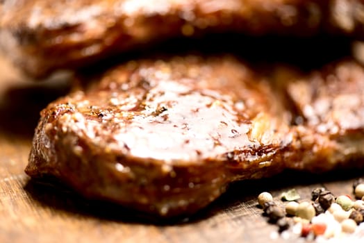 Succulent thick juicy portions of grilled steaks on an old wooden board with salt and pepper