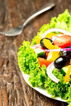 Salad with vegetables and greens in plate on wooden table