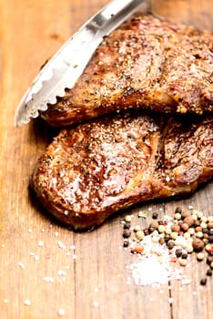 Succulent thick juicy portions of grilled steaks on an old wooden board with salt and pepper