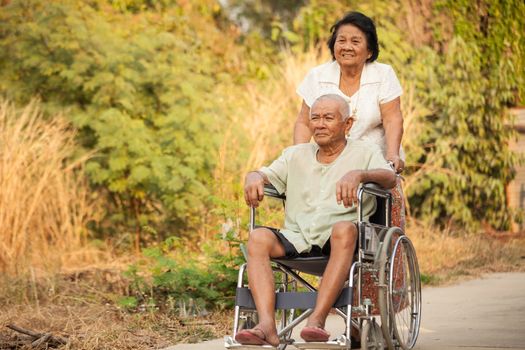 Asian senior woman pushing her disabled hasband on wheelchair