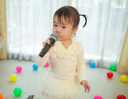 Happy little asian girl with microphone in the home