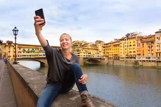Young lady taking selfie in front of Ponte Vecchio bridge in Florence Tuscany Italy, during her summer vacations in Europe.