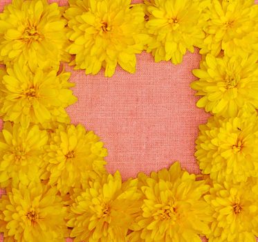 Frame of yellow flowers against a background of pink cloth                               