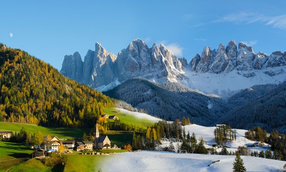 Composite image of two photos taken two days after one another showing the change of season from fall to winter. The village of St. Magdalena or Santa Maddalena with church in front of the Geisler dolomites mountain peaks in the Val di Funes in Italy.