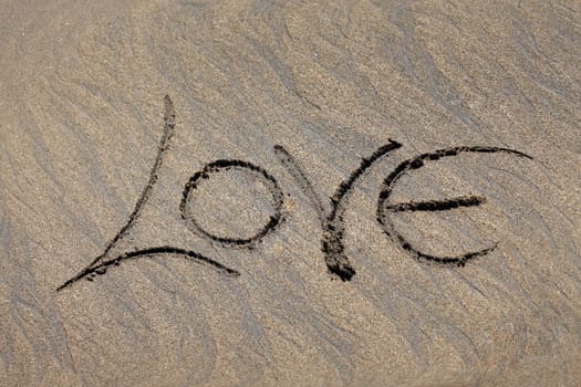 The word "love" is written by someone on sand