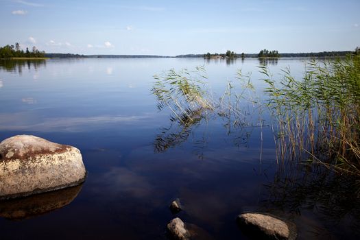 Water landscape with stones. Stones in water. The lake with stones. Beautiful landscape. Water smooth surface and the blue sky with clouds.