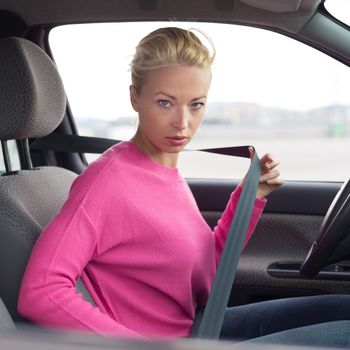 Safety first. Beautiful blonde caucasian lady fastening car seat belt.