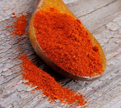 Crushed Paprika in Wooden Spoon closeup on Rustic Wooden background