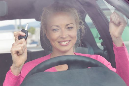 Woman driver showing car keys. Young female driving happy about her new car or drivers license. Caucasian model.