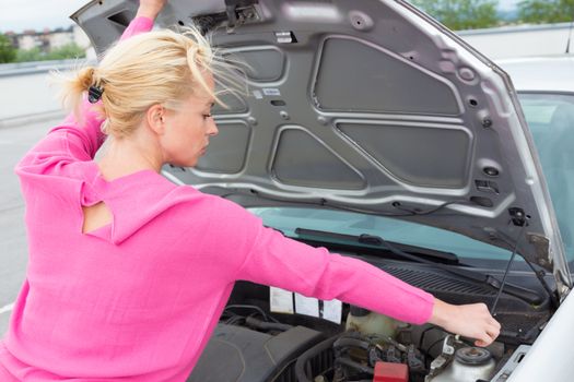 Self-sufficient confident modern young woman opens the hood of the car to inspect broken car engine.