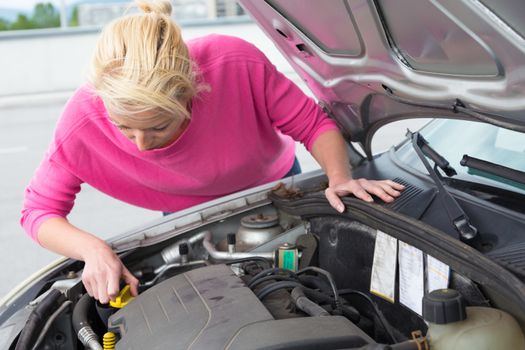 Self-sufficient confident modern young woman inspecting level of the engine oil in the car.