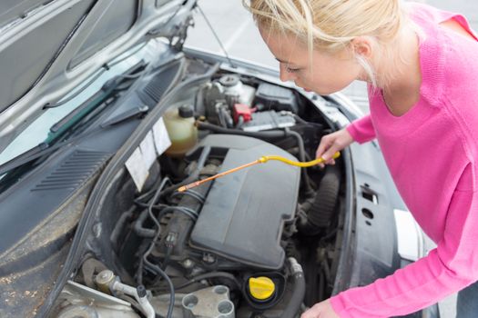 Self-sufficient confident modern young woman checking level of the engine oil in the car.