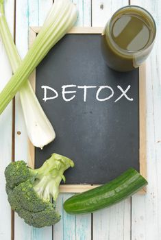 Detox handwritten on a blackboard with a green vegetable smoothie and ingredients