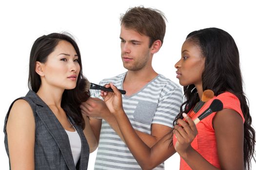 Assistants applying make-up to female model over white background