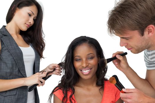 Assistants applying make-up to a female model over white background
