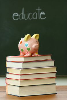 Piggy bank on a pile of books in front of blackboard 