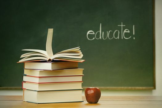 School books and apple on desk with blackboard in background