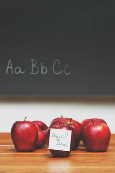Red apples with note on desk with blackboard in background 