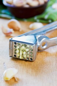 Garlic press with fresh garlic on wood