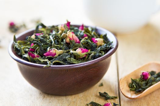 Green tea leaves with rose buds by tea pot