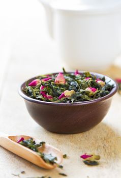 Green tea leaves with rose buds by tea pot