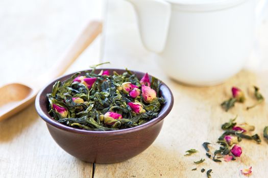 Green tea leaves with rose buds by tea pot