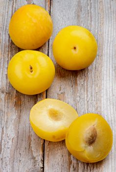 Arrangement of Ripe Sweet Yellow Plums Full Body and Halves isolated on Rustic Wooden background