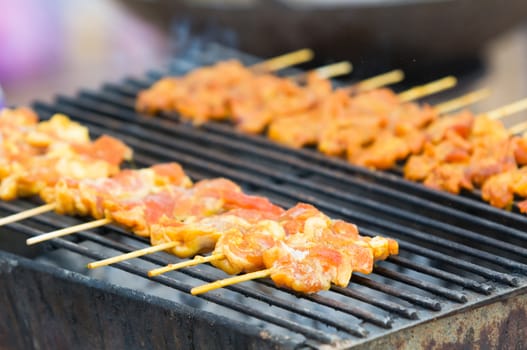 Pieces of pork on wooden sticks on a barbecue in Thailand. Very shallow depth of field with the nearest pieces of pork in focus.