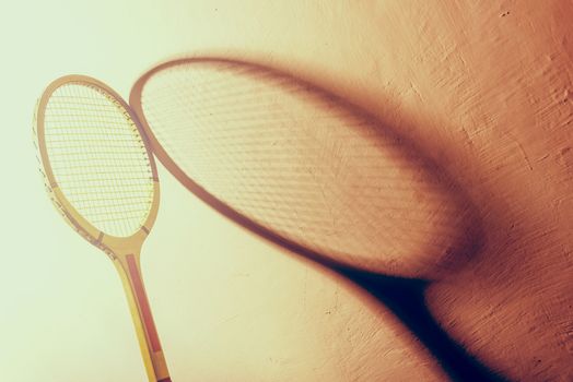 Backlit vintage tennis racket and its shadow