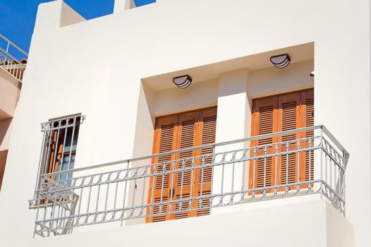 Fragment of a facade of the old house on the coast of the island of Crete with a balcony and ancient wooden blinds from the sun.