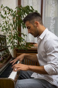 Young handsome male artist playing his wooden classical upright piano, indoor portrait