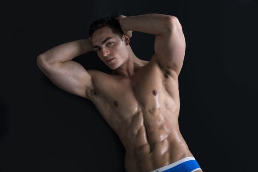 Attractive young man laying on the floor with naked muscular ripped body, hands under head