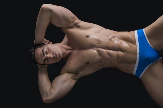 Attractive young man laying on the floor with naked muscular ripped body, hands under head