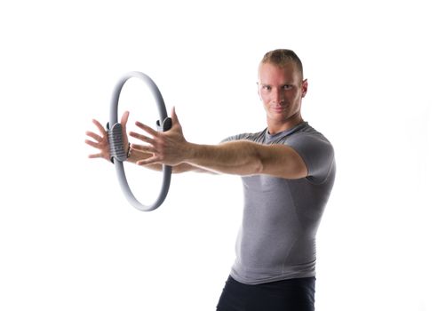 Young muscular man exercising with Pilates ring in front of chest, isolated on white