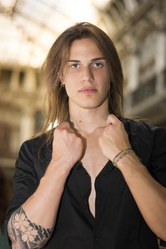 Handsome long hair man portrait in black shirt standing in elegant gallery in european city center