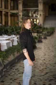Handsome long hair man portrait in black shirt standing in elegant gallery in european city center