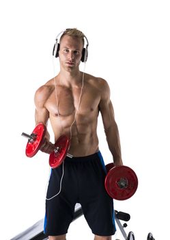 Portrait of a muscular blond young man lifting weights and listening to music in headphones, isolated over a white background